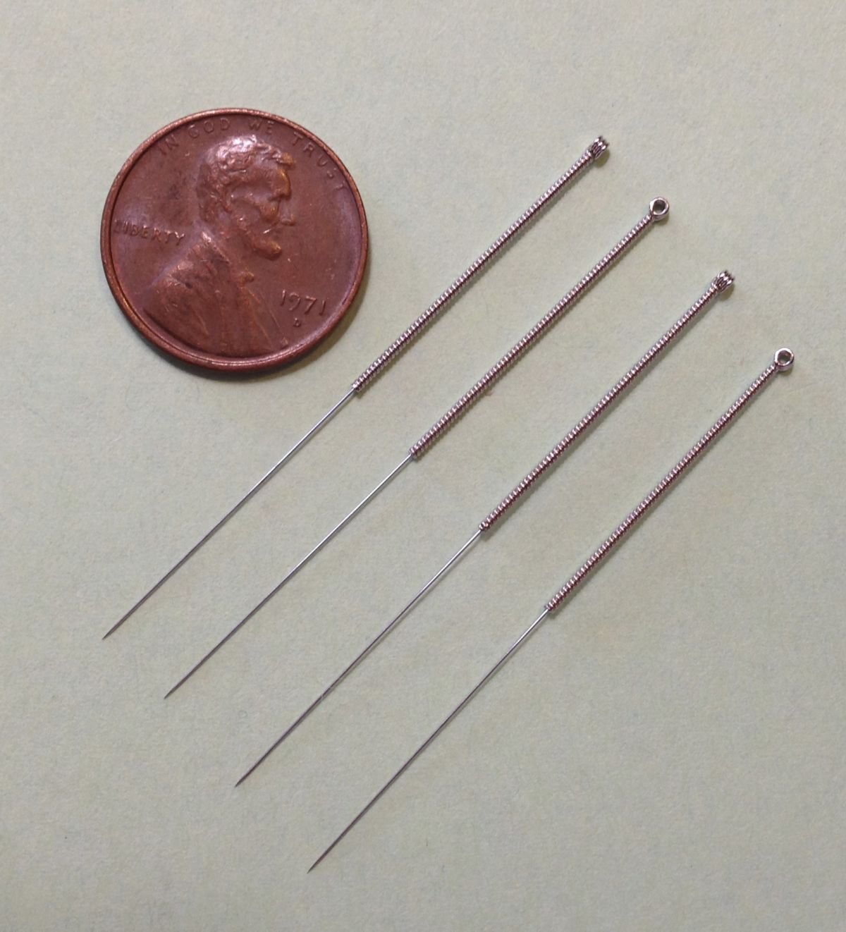 Four fine acupuncture needles beside a small coin, showing how thin they are