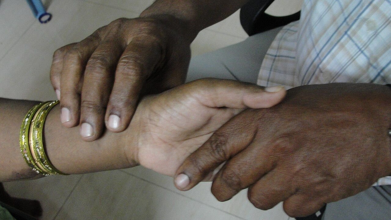 A practitioner’s fingers resting on a patient’s wrist to read the pulse